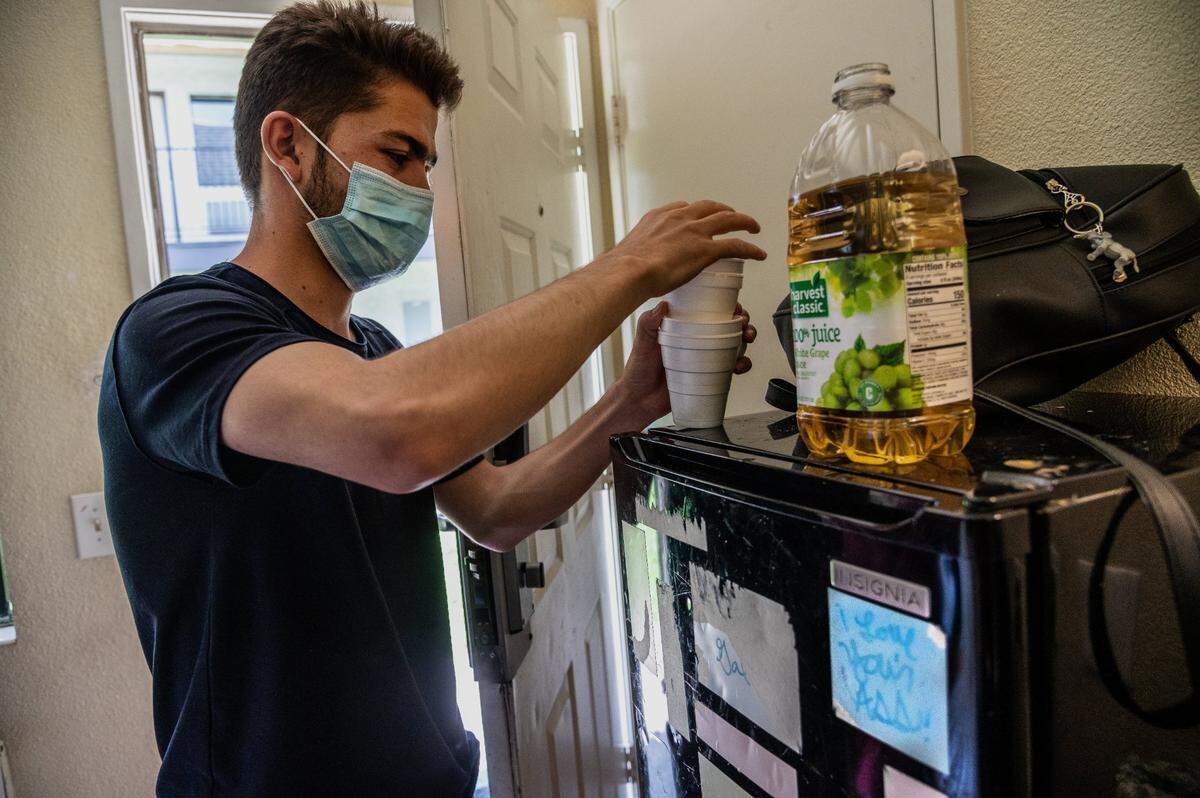 Rashed, 20, gets ready to pass out apple juice resting on a worn out refrigerator with a label that reads “I love your ass,” inside America’s Best Value Inn a few days after arriving in Sacramento. He said he is studying for a drivers license exam on a mobile phone app.