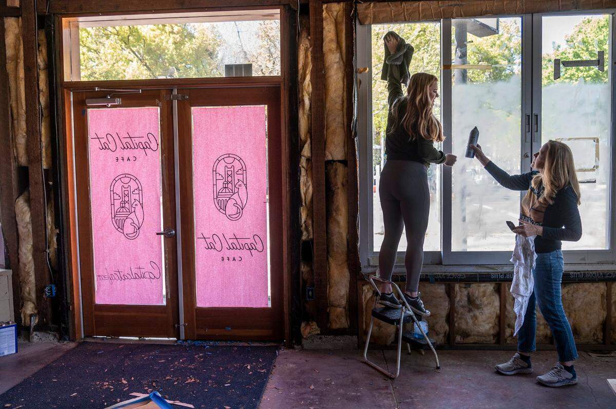 Emalee Ousley, left, and her mom Laura Ousley, right, co-owners of Capital Cat Café, clean windows on Tuesday, March 22, 2022. They were placing signage on the doors and windows of the cat cafe that will open in the fall in Midtown, Sacramento. The wine, beer and coffee lounge will also have small bites to eat with a separate space for customers to spend with cats that need adoption.