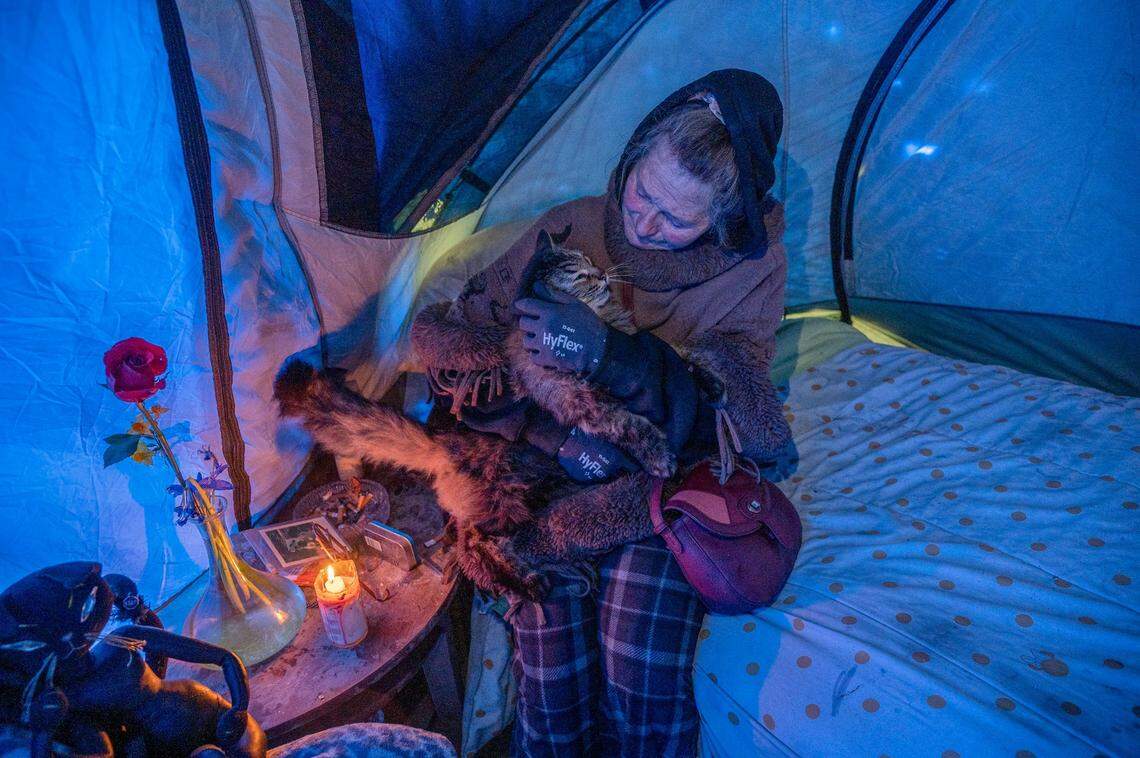 Catherine Roberts caresses her cat “Smokey” as a candle flickers inside her tent in the Bannon Island encampment on Feb. 23. Her generator is broken and she doesn’t have lights or heat. She worries she will never find an affordable apartment with her pets.