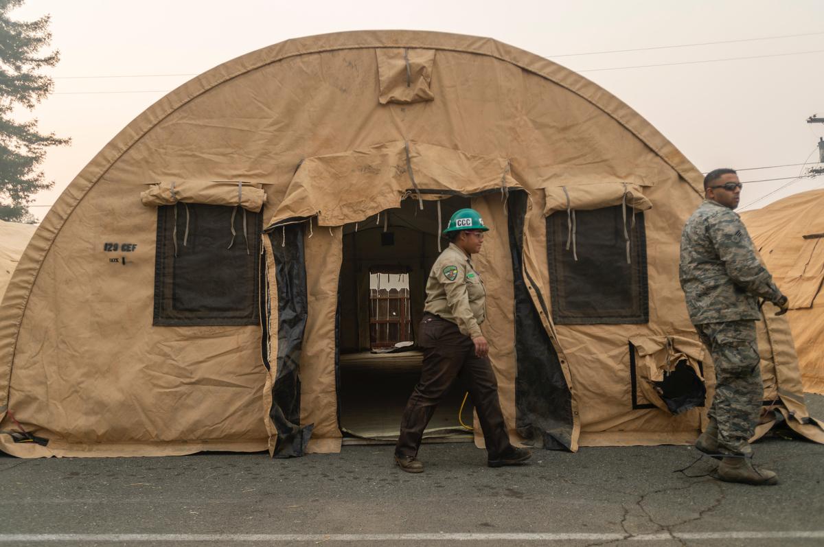 Enafaye Nine-Rowe, a member of Chico California Conservation Corps, and California Air National Guard Sgt. Manghirmalani walk past an isolation tent at East Ave Church in Chico on Friday.