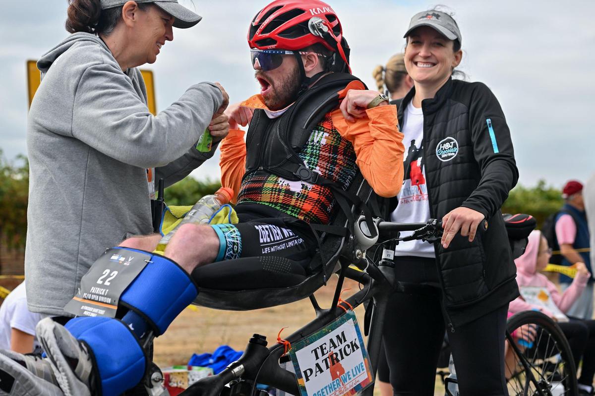 Sara Keeling, left, helps Patrick Utitus-Canez from Gilbert, Ariz., with applesauce while Lauren McGuire helps steady the bicycle at about the 38-mile marker on the bike course during the Ironman California triathlon on Sunday. Utitus-Canez, who has cerebral palsy, is participating in his fifth Ironman.