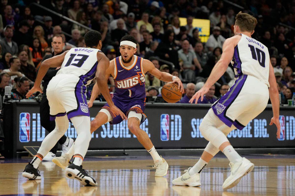 Phoenix Suns guard Devin Booker (1) drives between Sacramento Kings forward Keegan Murray (13) and center Domantas Sabonis (10) in the first half Tuesday, Feb. 13, 2024, at Footprint Center in Phoenix, Arizona.