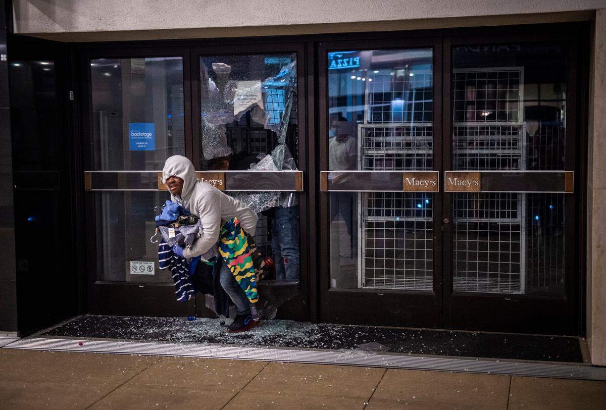 A looter comes through broken glass doors at Macy’s with a handful of goods after a long day of protests turned violent on May 30, 2020, in downtown Sacramento after the death of George Floyd in Minneapolis.