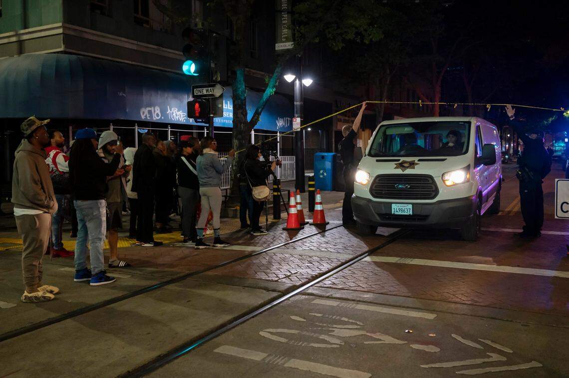 A coroner’s van leaves the mass shooting scene at 9th and K streets after 9 p.m. while community members stand at the corner on Sunday night in downtown Sacramento.