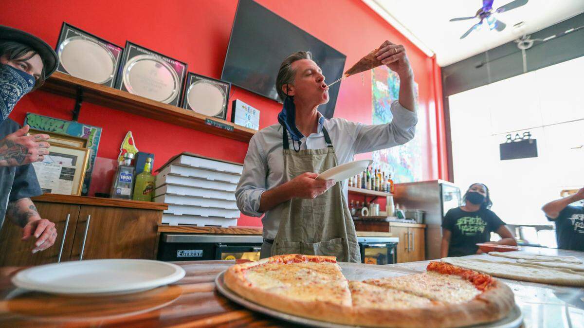 Graffiti Pizza executive chef Matt Molina, left, looks on as California Gov. Gavin Newsom tries a slice of pizza during a visit in Oakland, Calif., on Thursday, June 17, 2021. A man has been arrested on suspicion of assaulting Newsom during his visit to downtown Oakland, authorities said Friday, June 18. Newsom was walking to a barbershop and pizzeria in Old Oakland to promote small businesses when he was “approached by an aggressive individual,” said Fran Clader, director of communications for the California Highway Patrol, which provides security for the governor. (Ray Chavez/Bay Area News Group via AP)