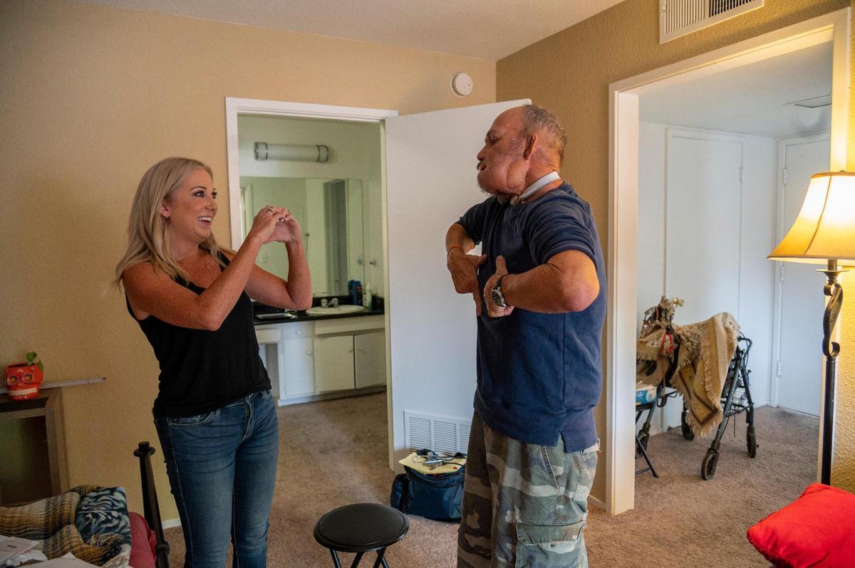 Meitra Bozorgzadegan, left, and Jim Wilson signal hearts to each other Friday in an apartment she helped him find. She befriended him after he had been homeless for 15 years and helped him through throat surgery for cancer and to find affordable housing.
