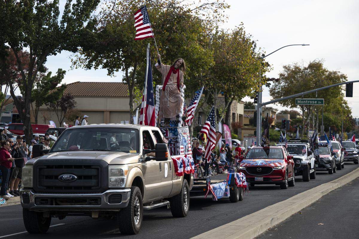 A man dressed as Jesus carries the American flag as the Freedom Riders 1776 drive down East Bidwell Street during a Veterans Day parade in Folsom on Tuesday, Nov. 11, 2025.