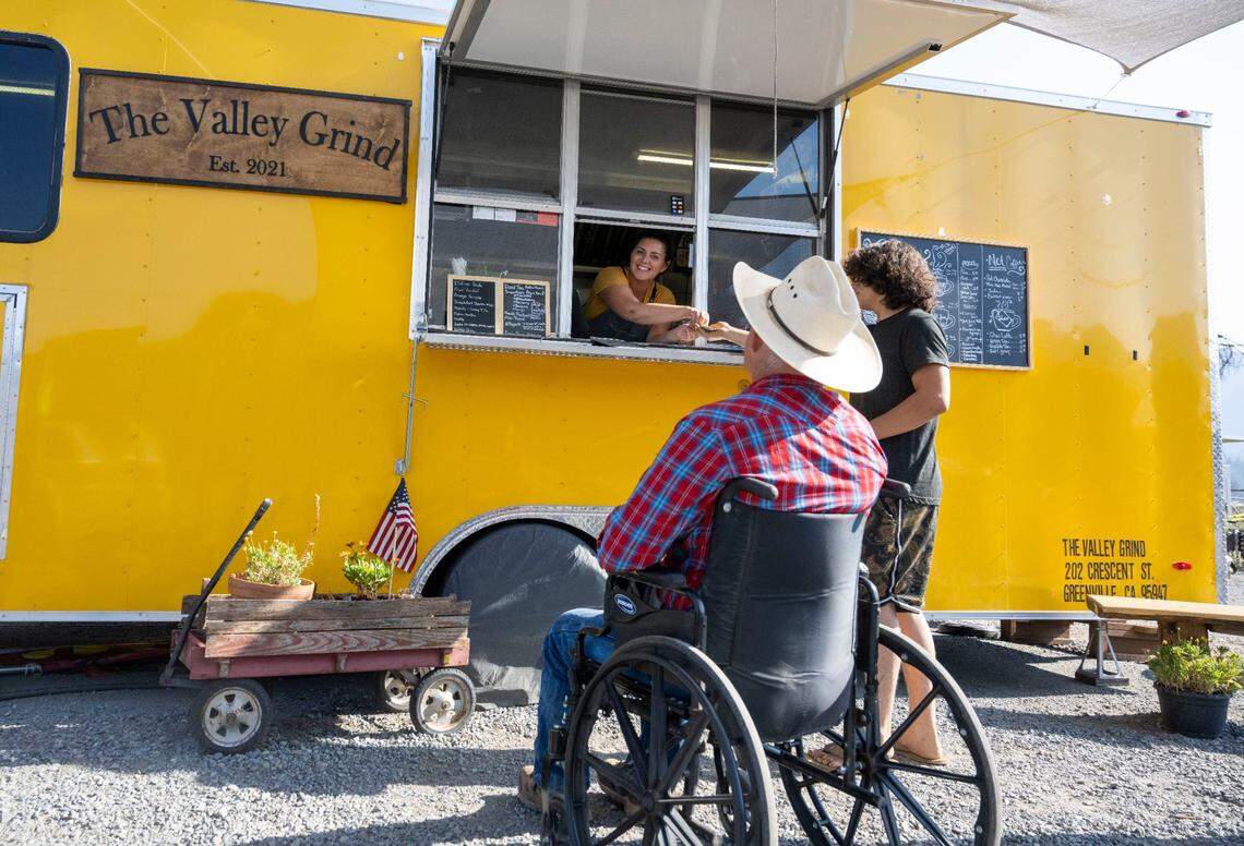 Rachel Goings, owner of The Valley Grind, hands out change to a customer on Thursday as she prepares to take an order from customer Robert Copeland. Goings was getting ready to roll out the red carpet for the grand opening of her new coffee shop when the Dixie Fire burned down her business a year ago.