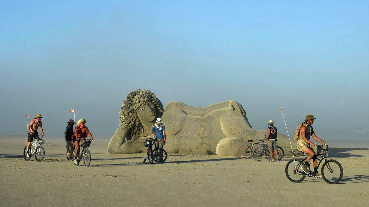 Burners ride their bikes near an art piece during Burning Man on Saturday, Aug. 27, 2022, near Gerlach, Nevada.