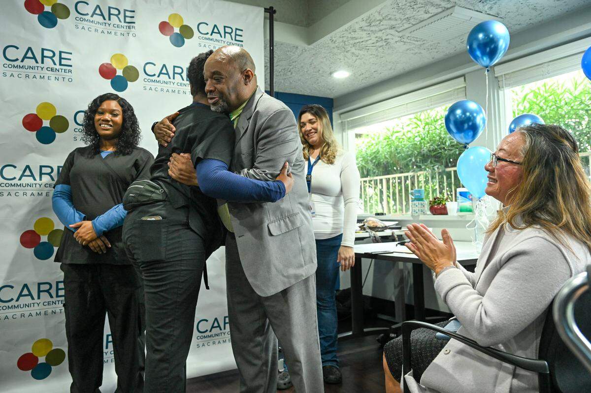 Kathy Chao Rothberg, right, CEO of Lao Family Community Development, claps as Maurice Harper, founder and teacher of TSQ Nursing Academy, hugs a student during a March ceremony for graduates of their certified nursing assistant program at the former Vagabond Inn. The motel was transformed by Rotherg’s organzation into a campus devoted to assisting homeless people find work and housing.