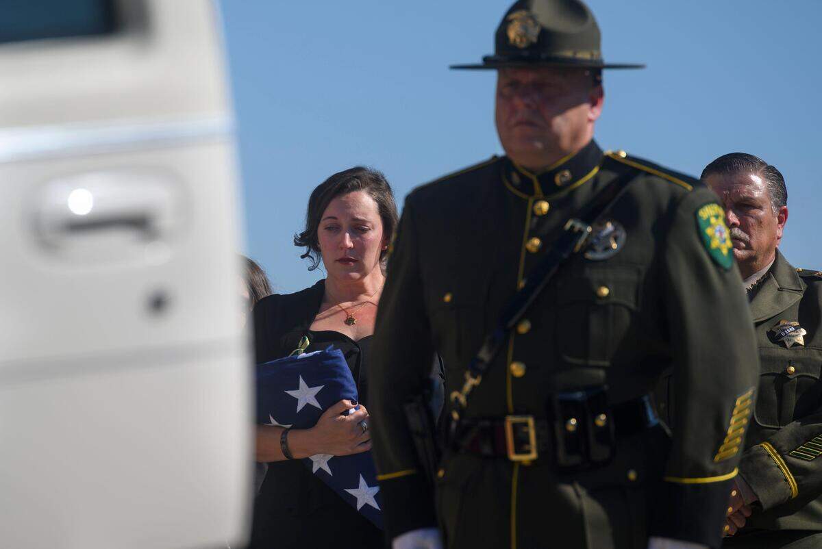 18. Katie Kregoski Ishmael, left, wife of fallen El Dorado County Sheriff’s Deputy Brian Ishmael, holds a flag while her husbands casket is placed in a hearse at Bayside Adventure Church in Roseville, Tuesday, Nov. 5, 2019. El Dorado County Sheriff John D’Agostini stands at the far right.