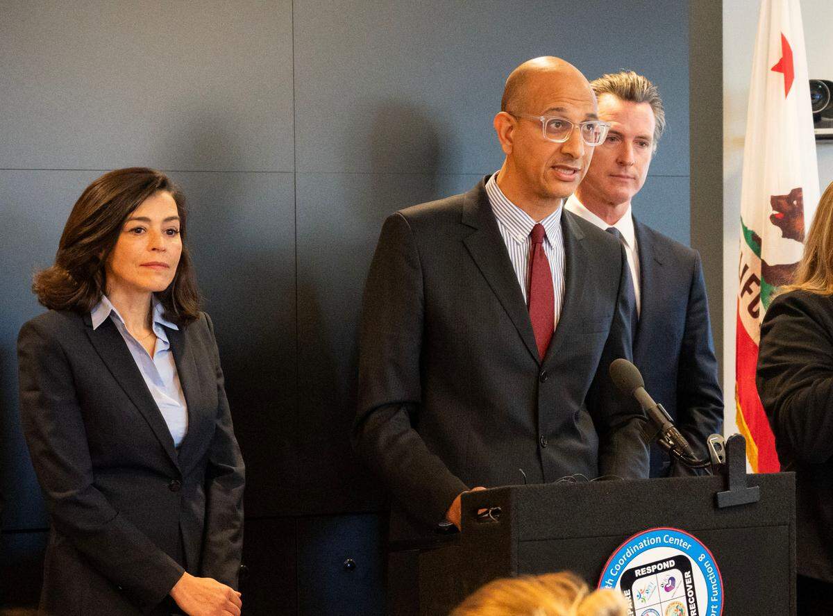 Dr. Mark Ghaly, secretary of the California Health and Human Services Agency, center, joined by Gov. Gavin Newsom and then-Department of Public Health Director Sonia Angell, speaks at a press conference on Feb. 27, 2020, about a patient at UC Davis Medical Center who contracted the coronavirus in Solano County a few weeks before the governor's stay-at-home order. 