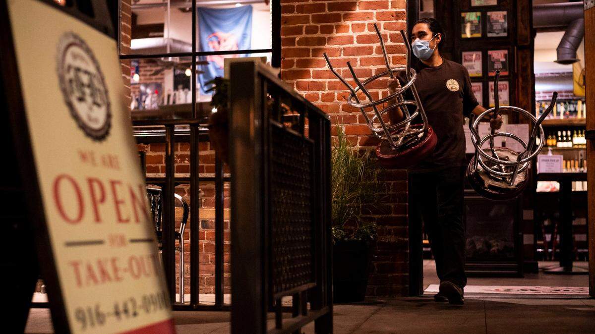 Manuel Gomez, a server at Burgers and Brew in midtown Sacramento, takes stools and chairs outside for diners Tuesday, Jan. 12, 2021, after the state announced the stay-at-home order was lifted for the greater Sacramento region. The move back into the purple tier was a result of new data that show hospitals likely will not be as crowded with COVID-19 patients in the coming weeks, according to Gov. Gavin Newsom.