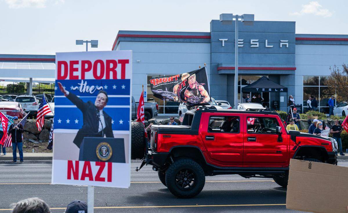 Anti-Tesla demonstrators wave signs across the street from the Tesla dealership in Rocklin as Trump supporters counterprotest across the street and a truck drives by with Trump flags on Saturday, March 29, 2025.
