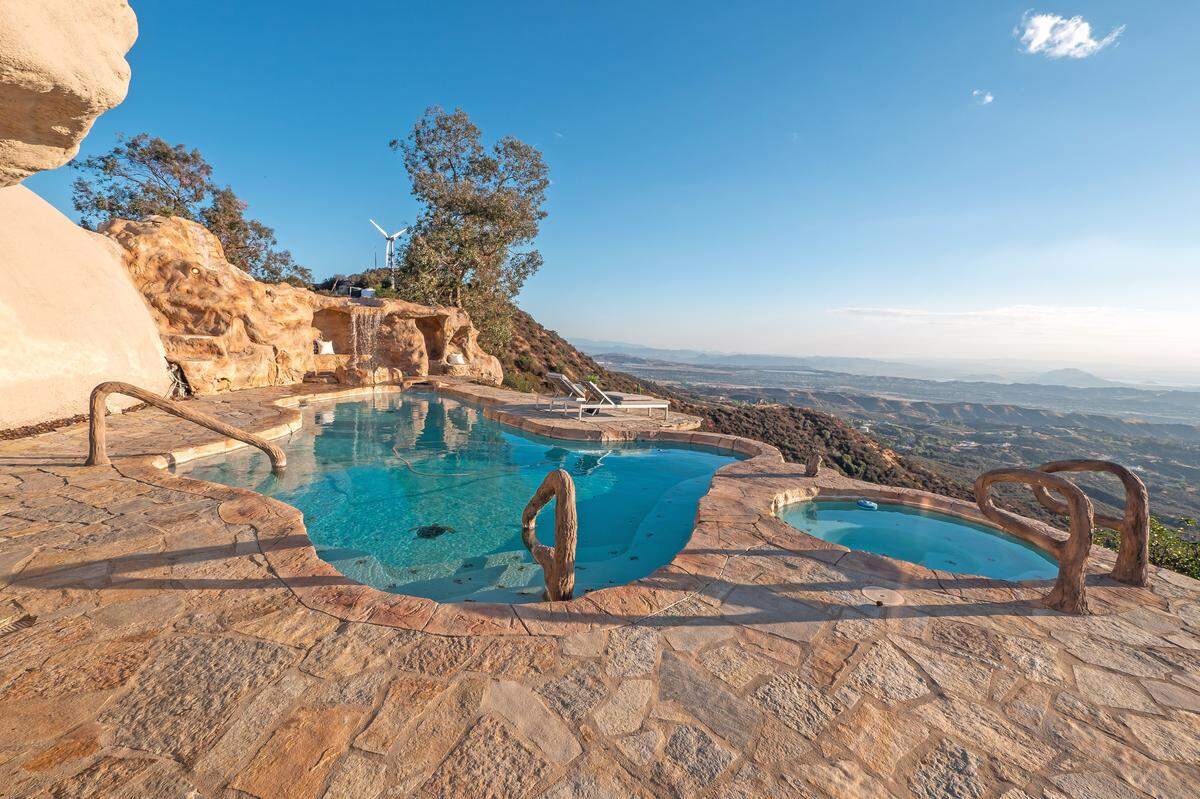 The property features an exotic swimming pool with a dramatic waterfall and hidden grotto, plus two spas—an in-ground spa and an additional above-ground spa on the expansive viewing deck for soaking while taking in the mountain views.