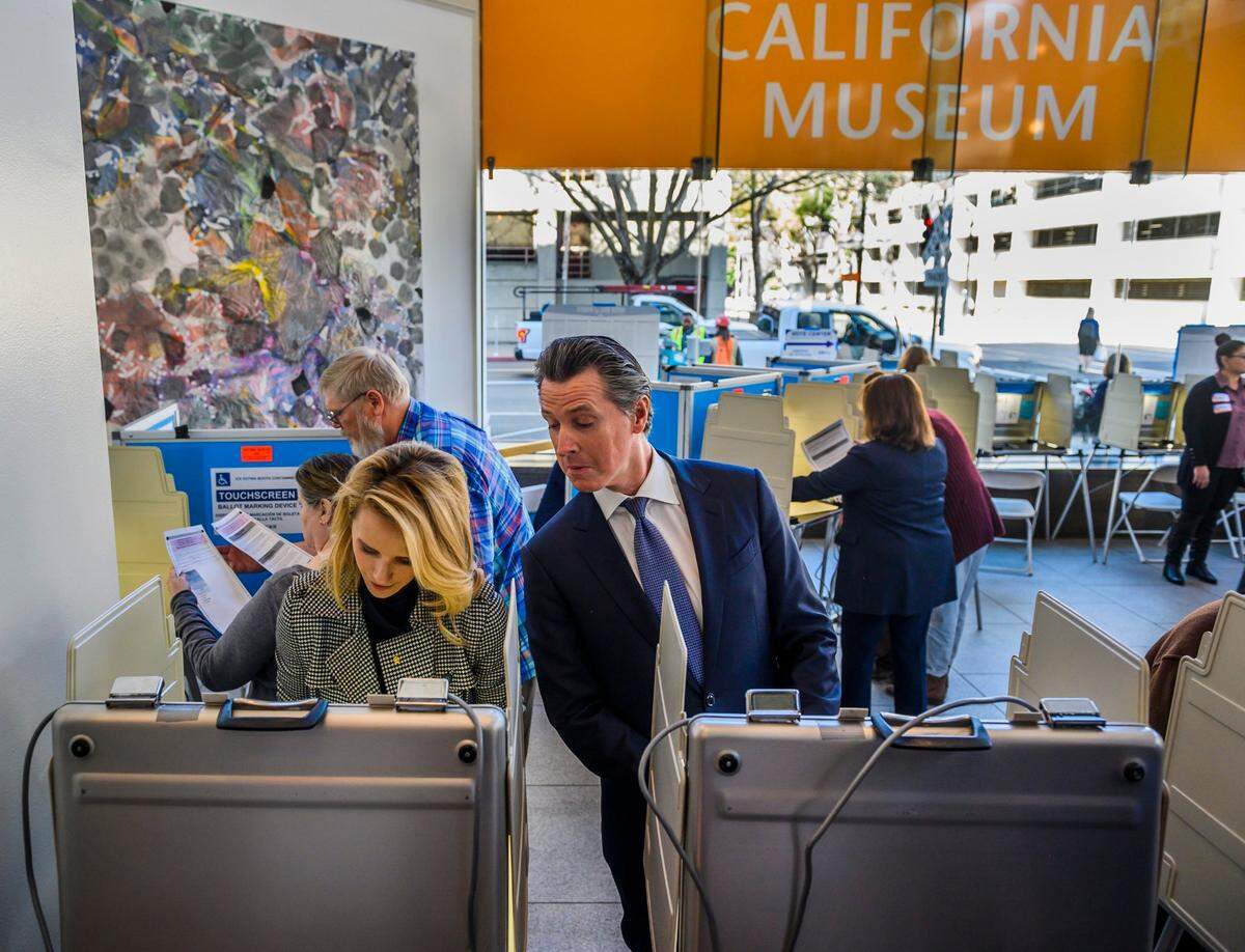 California Gov. Gavin Newsom jokingly peeks over the shoulder of his wife, First Partner Jennifer Siebel Newsom, as they vote during the primary election on Super Tuesday at the California Museum in Sacramento on March 3, 2020.