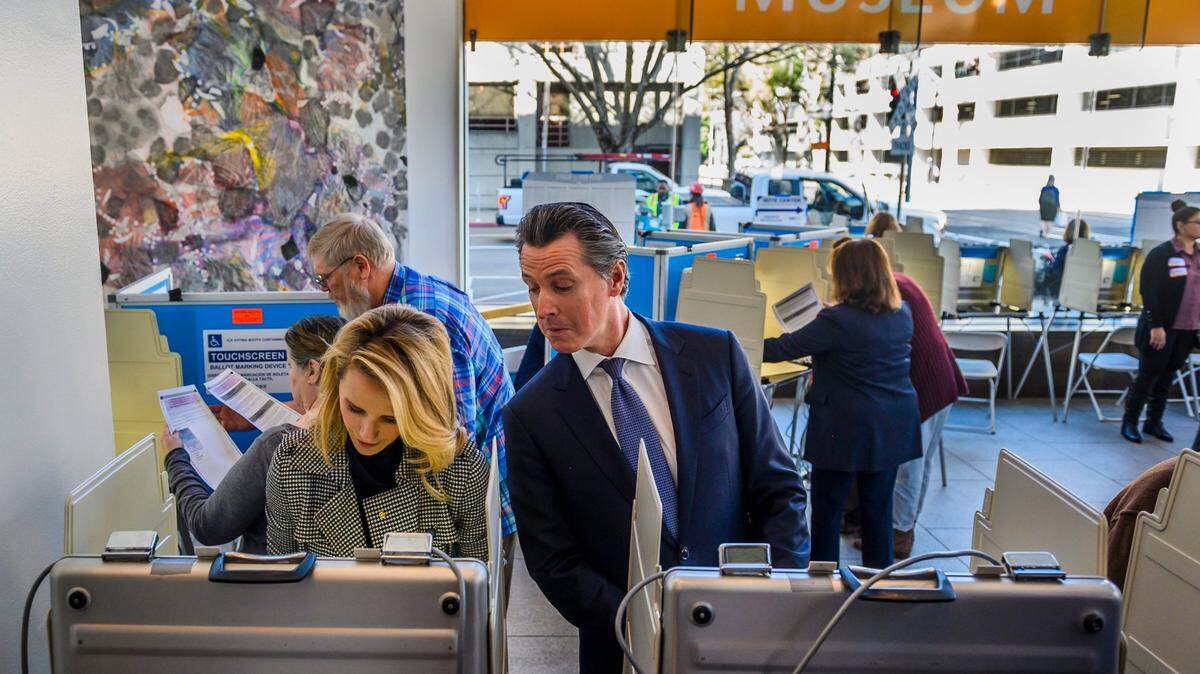 California Gov. Gavin Newsom jokingly peers over the shoulder of his wife, First Partner Jennifer Siebel Newsom, as they vote during the primary election on Super Tuesday at the California Museum in Sacramento on March 3, 2020.
