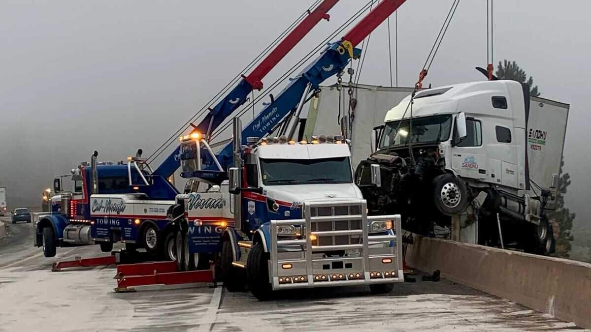 Heavy duty tow trucks recover a damaged tractor trailer left teetering on a concrete barrier after a crash involving two big rigs on eastbound Interstate 80 near Truckee on Tuesday, July 14, 2026.