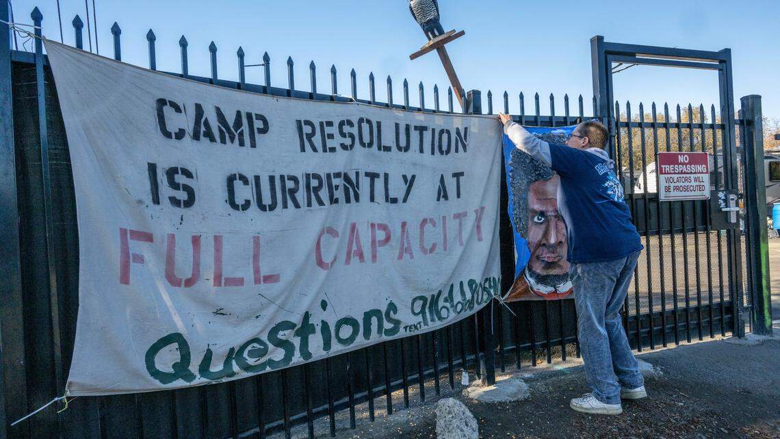 Sharon Jones adjusts a banner Wednesday, Dec. 13, 2023, outside the security gate of Camp Resolution, a self-governing homeless encampment she co-founded with her wife Joyce Williams on a lot they leased from the city of Sacramento in April. They said there is a waiting list of 800 people to get into the camp, which is full to capacity. “We need to pull the homeless into camps or put them in housing,” said Jones.