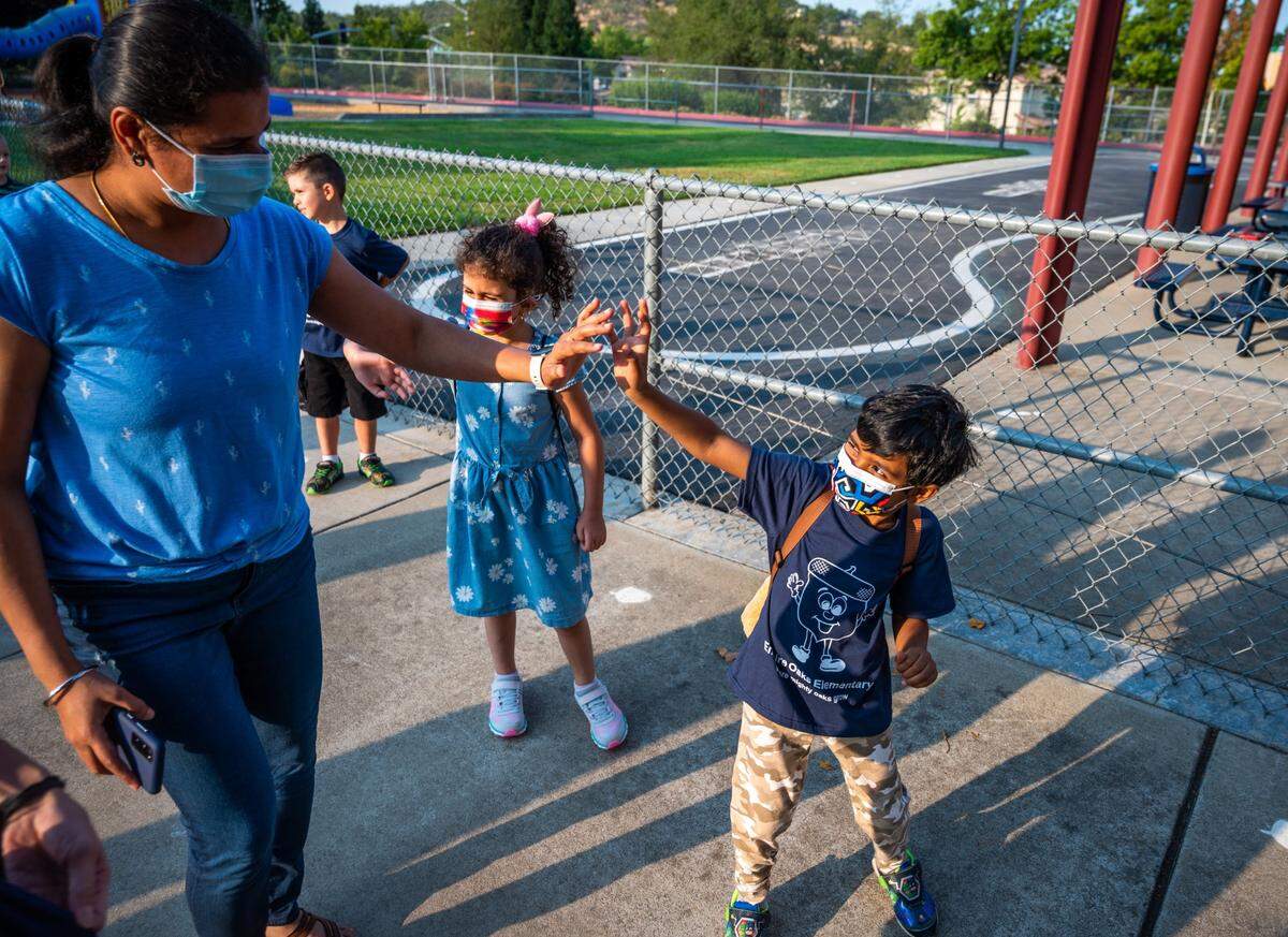 Kindergartener Tharun Prakash waves at his mother, Yuvarani Ayyasamy, as he goes into his first day of school at Empire Oaks Elementary School in Folsom on Wednesday, Aug. 11, 2021. We are following the current guidelines — which are masks indoors and, you know, we will eat lunch outside as much as possible. But when we are inside for lunch, we will practice some safety measures like distancing,” said Principal Sara Parenzin of Empire Oaks Elementary School.