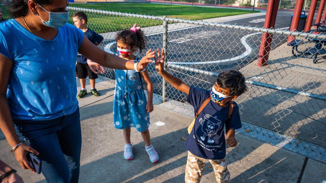 Kindergartner Tharun Prakash waves at his mother, Yuvarani Ayyasamy, on his first day of school at Empire Oaks Elementary School in Folsom on Wednesday, Aug. 11, 2021. Some school districts in California still require children wear masks during outdoor activities, including recess.