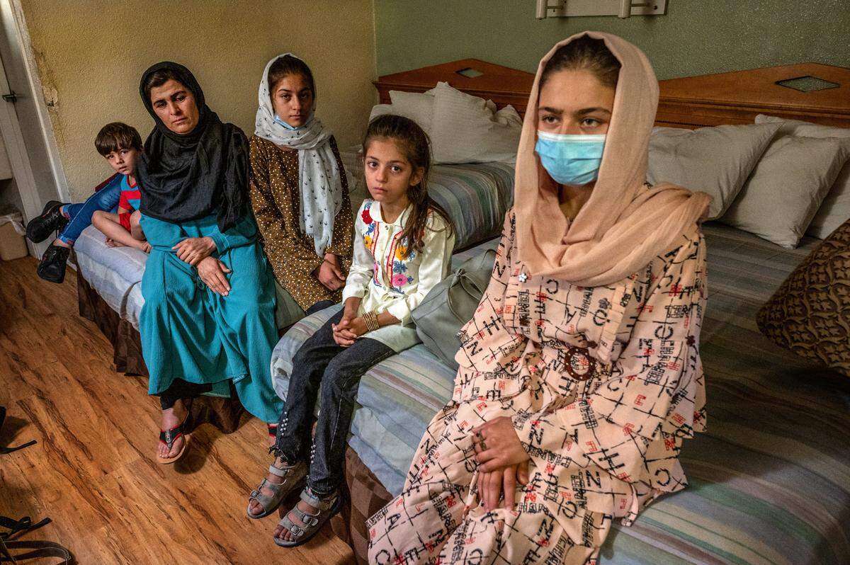 On their first night in the United States, Abdul’s family sits on the beds in a motel room in North Highlands on Monday, Aug. 16, 2021, after traveling from Afghanistan. The battered room had no towels, soap or toilet paper upon their arrival. By custom, the family would take their shoes before entering a living space, but they chose not to after seeing the room’s condition.