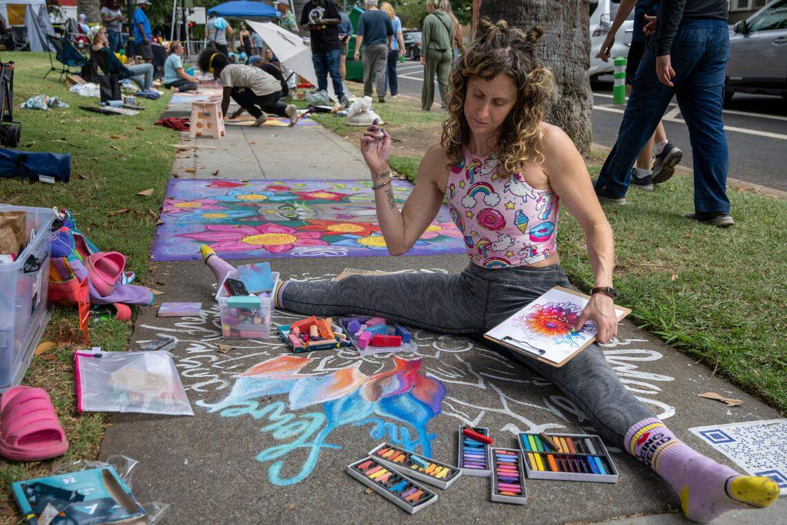 Artist Stacy Frank sits in the middle of her sidewalk art that says, “The flower doesn’t dream of the bee, it blossoms and the bee comes,” during the Chalk It Up festival on Saturday, Sept. 2 at Fremont Park.
