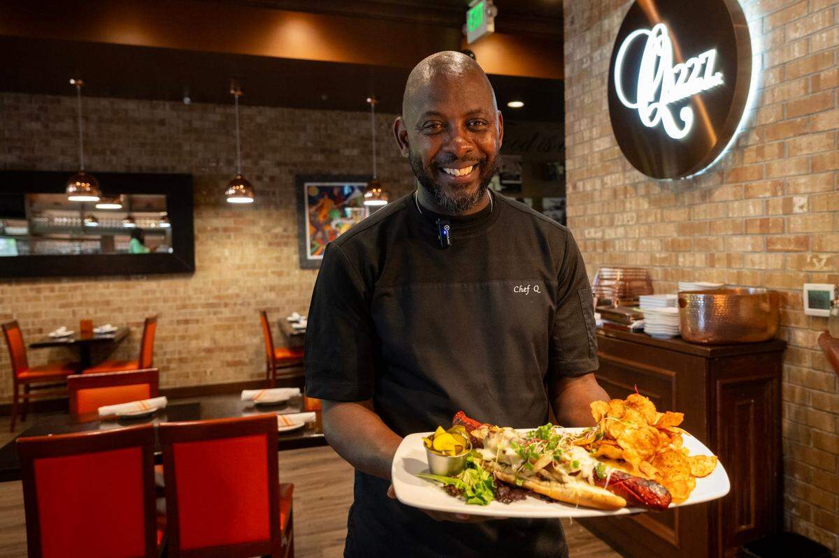 Chef Quentin Bennett holds the Q-dog, a wagyu beef hot dog served with bone marrow aioli, onion, jalapeño, bacon jam, fontina cheese, house pickles and seasoned potato chips, at Q1227 on Friday.
