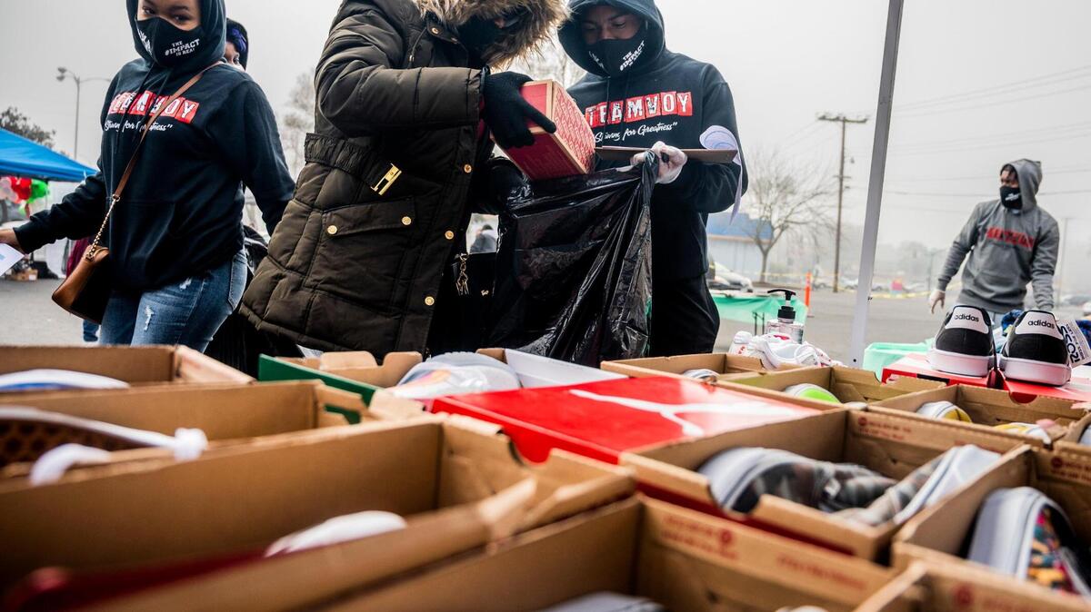Lorraine Juniel, 30, of Sacramento, hands volunteer Joshua Hamilton a pair of shoes at a gift giving event in front of Hidden Gems Thrift Store in Sacramento on Sunday, Dec. 20, 2020. The Voices of the Youth non-profit organization received the donations, giving away more than two thousand holiday gifts to families. Juniel is receiving the present to give to her kids for the holidays.