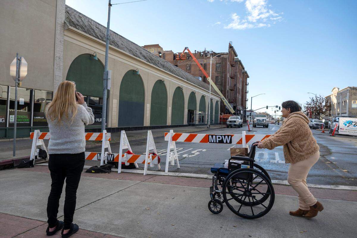 Mary Jane Mathews crosses the street as Dee Hanson views construction workers remove the top layer of freestanding bricks at the Hotel Marysville on Thursday before demolition begins next week.