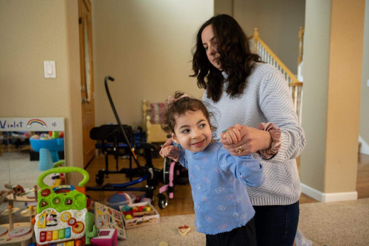 Frances Pimentel helps her 3-year-old daughter, Violet, walks in the living room at home earlier this month in Folsom. The family relies on multiple state and federal services to help care for their handicapped child. 