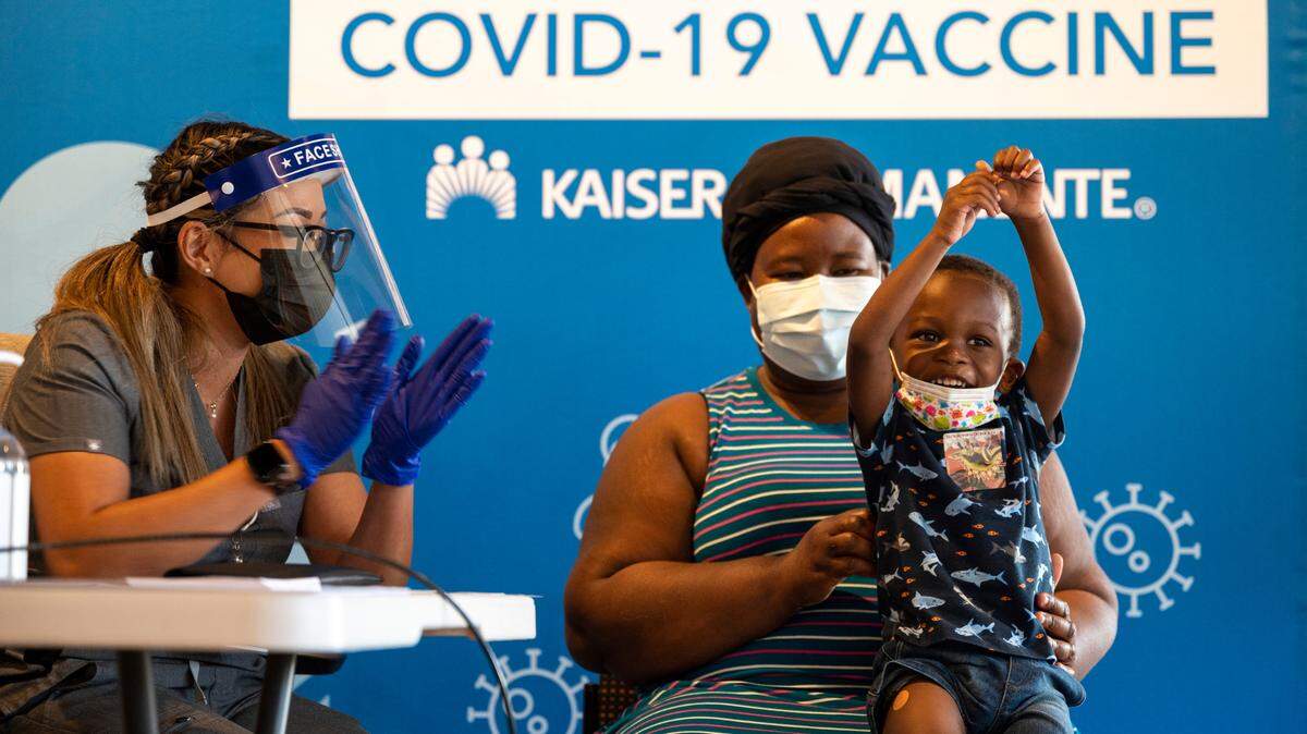 Bryan Yeboah, 3, celebrates after receiving the Moderna COVID-19 vaccination in his thigh from nurse Joanna Marie Pamintuan while being held by mother Perpetual Yeboah at the Kaiser Permanente Bruceville Center Vaccination Clinic in Sacramento on Thursday. Children ages six months to five years began receiving the inoculations at the clinic on Wednesday, after the recent recommendation by the Centers for Disease Control.