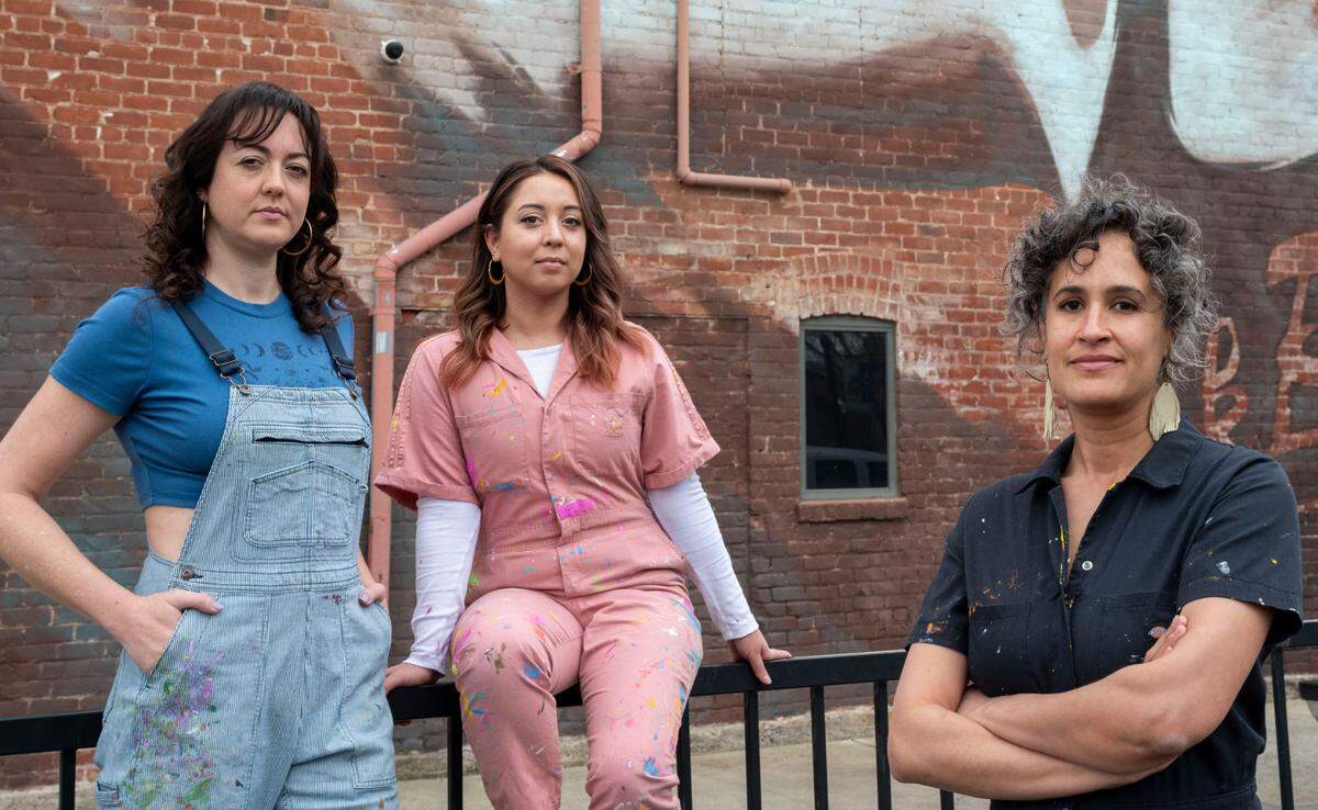 Sacramento artists, Jolene Rose Russell, left, Uli Smith, center and Jaya King stand in front of a mural March 22 on Oak Park’s Guild Theater done for Wide Open Walls in 2018. They claim the organization exploits new artists by underpaying them.