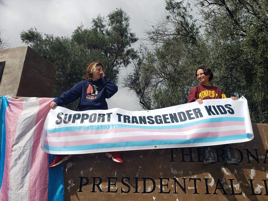 Ventura County residents Finn Samson and Sabrina Silva hold a sign that reads “Support Transgender Kids” next to a transgender pride flag at a protest against Florida Gov. Ron DeSantis outside the Ronald Reagan Presidential Library & Museum in Simi Valley on Sunday.