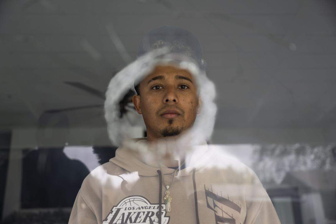 Brandon Hernandez, 26, looks Monday through a bullet hole in a window in the back of his house after a mass shooting near Stockton days before. Hernandez said he was working on his house when the shooting took place and he and his wife ran to a shed in the backyard as their house was sprayed with bullets.