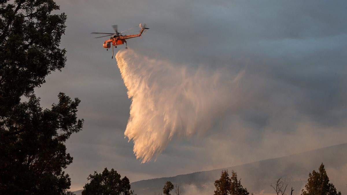 An air attack helicopter drops water on hot spots battling the Lava Fire in 2021, outside of Weed in Siskiyou County. A 2018 law temporarily protects homeowners in the area from being dropped by their insurers.