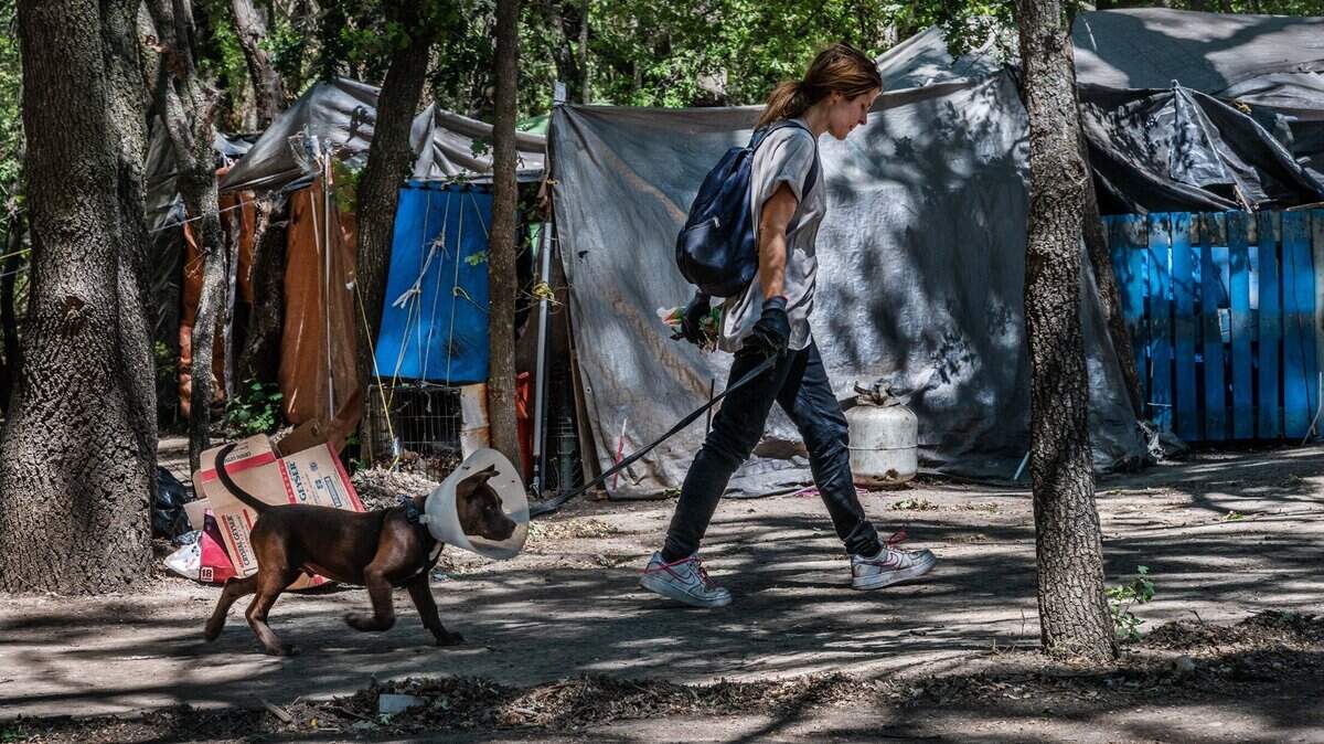 Rachelle Beck, 37, walks with her dog Bubba inside a homeless encampment near Discovery Park along the American River on Tuesday, June 8, 2021, in Sacramento. She had just helped deliver supplies to the elders that a volunteer had dropped off. She has been living in the encampment for the past 14 years she said.
