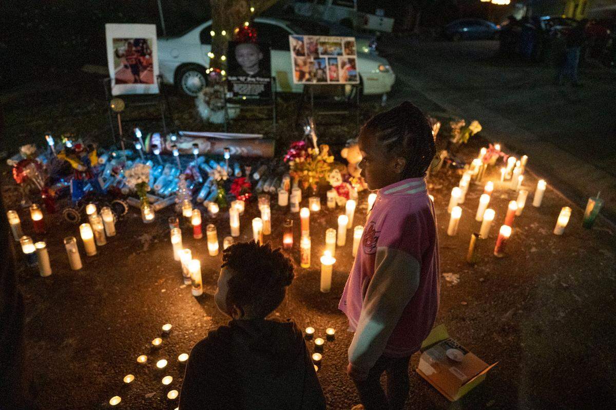 Children attending a vigil for Keith “KJ” Frierson on Tuesday stand near a memorial at the Hillsdale Oaks condo community, one month after he was shot and killed there on Dec. 30.