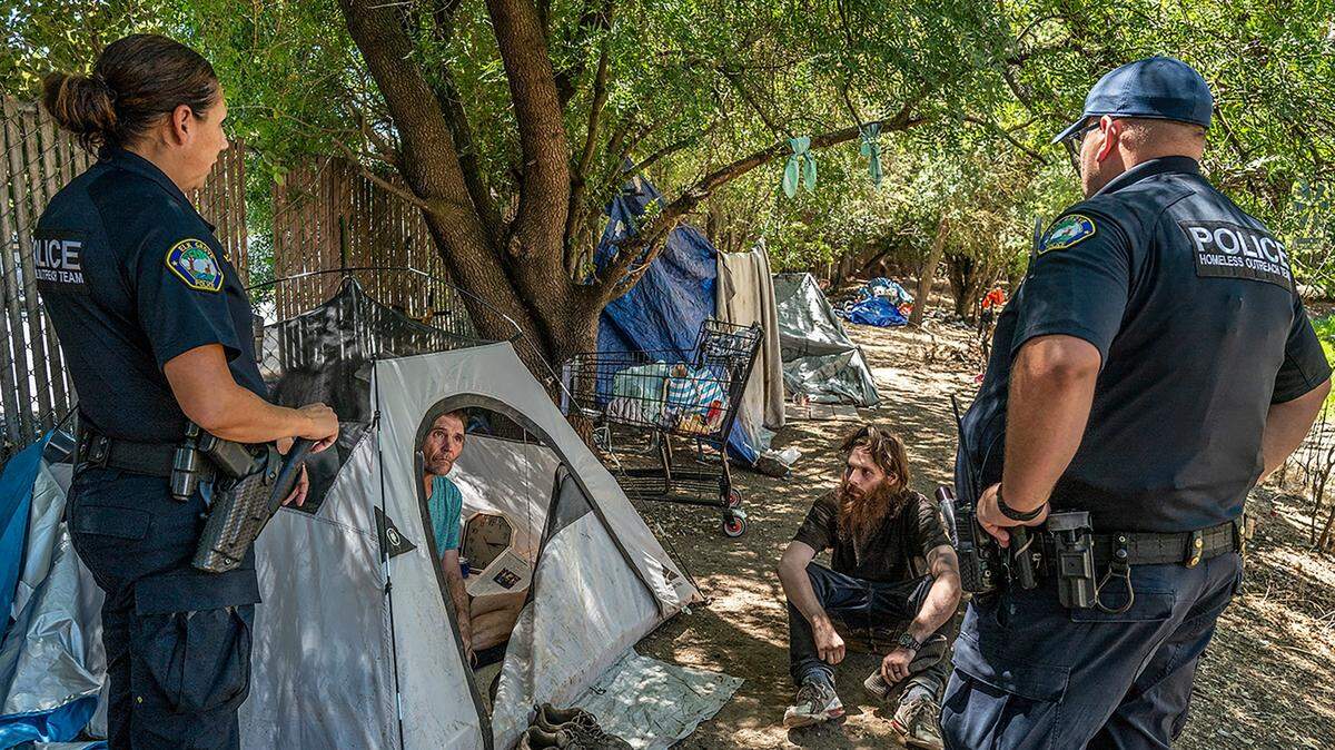 Homeless outreach officers Jennifer McCue, left, and Chris Cahill with the Elk Grove Police Department talk with homeless campers Jason, who did not want to give his last name, inside tent, and Allen Buchman, seated, in Elk Grove on Tuesday, July 19, 2022. A new city ordinance will clamp down on homeless campers. It bars the unhoused from camping within 500 feet of daycare centers, schools, playgrounds or youth centers; bans encampments without permitted electric, water and sewage hookups; and prohibits camping on private property without the property owners permission.