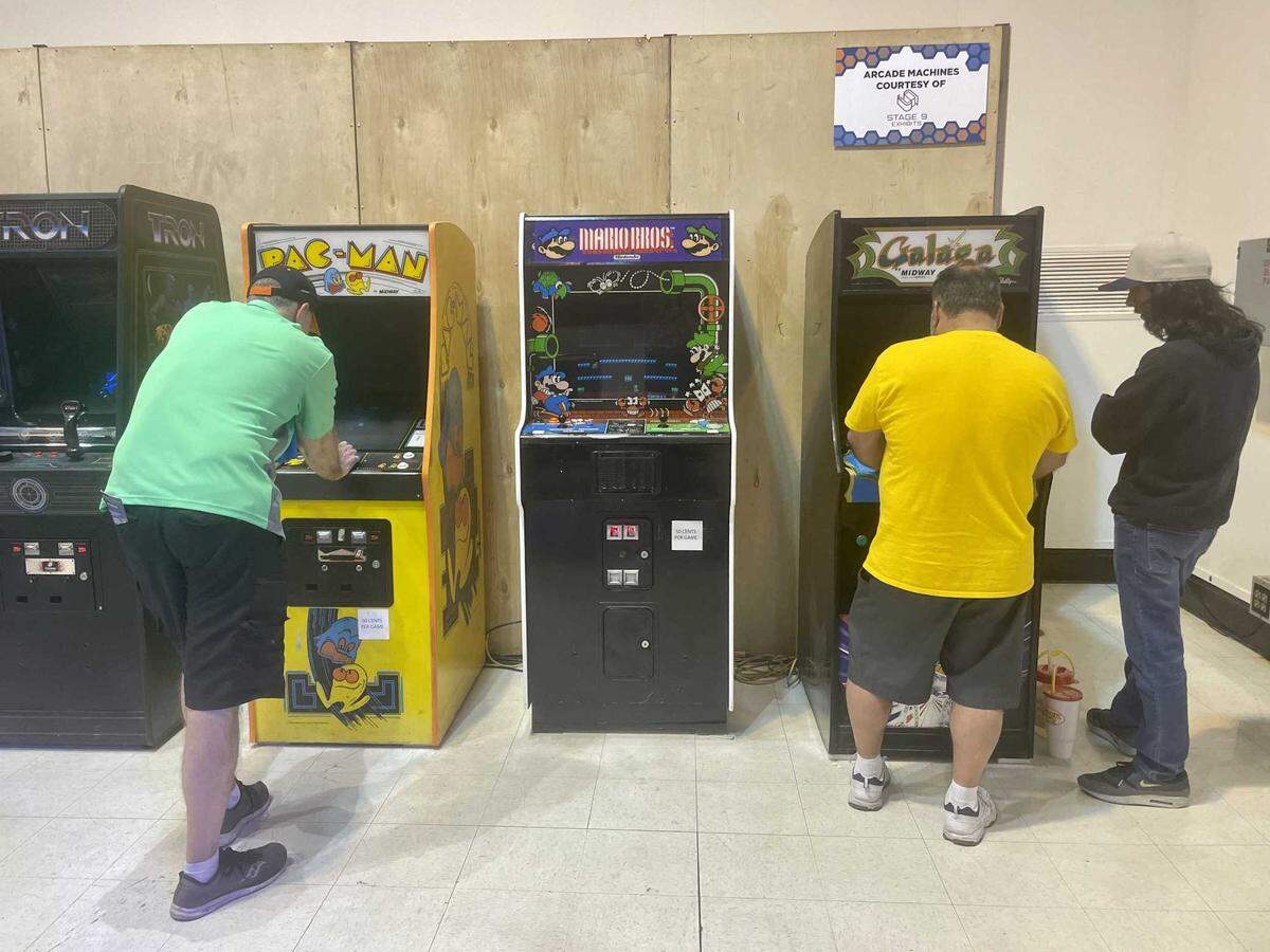 Fox Hamilton, left, and Dan Leon, center, compete on Pac-Man and Galaga during the Arcade Game Gauntlet, while Leon’s son, Dan Leon Jr., watches. The tournament Monday was played on these two machines, as well as Mario Bros.