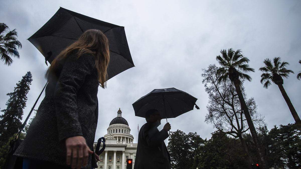 People hold umbrellas while passing the State Capitol while it rains on Tuesday, January 15, 2018.