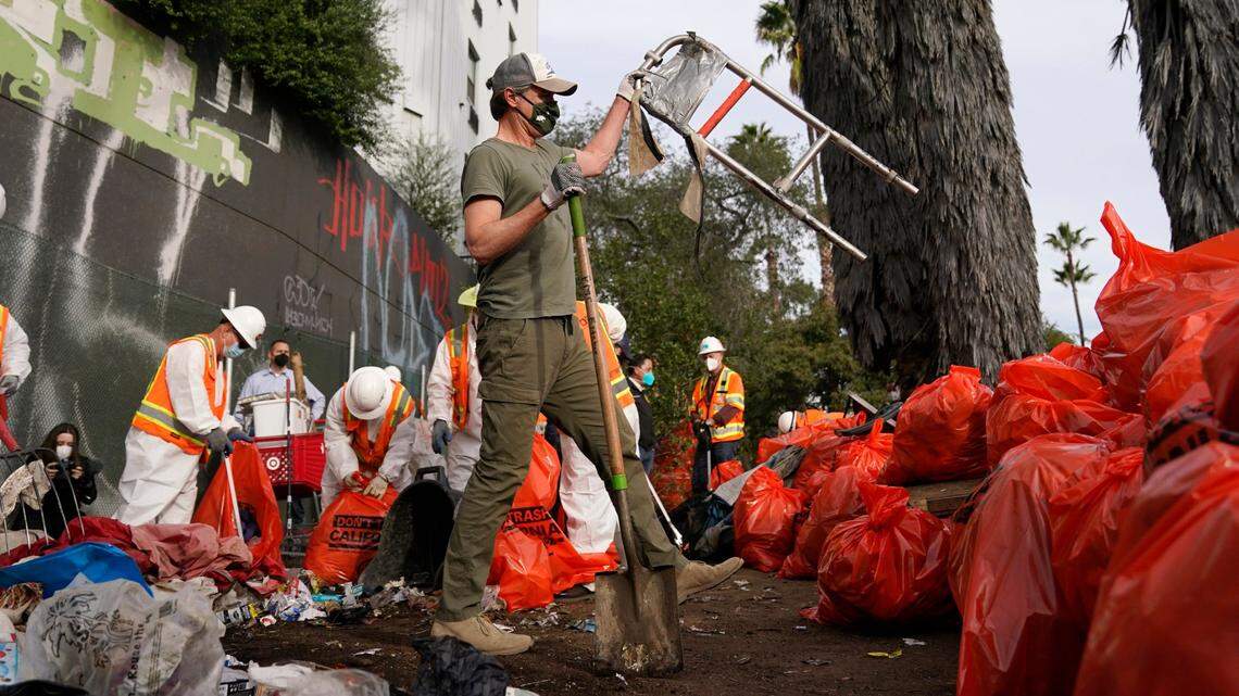 California Gov. Gavin Newsom, center, helps clean a homeless encampment alongside a freeway Jan. 12, 2022, in San Diego.