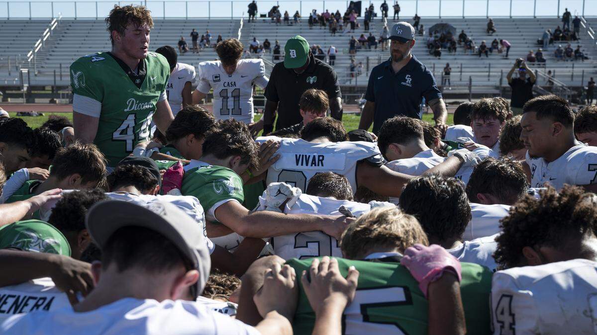 Members of the Dixon High School football team pray alongside members of the Casa Roble team after a game in Dixon on Saturday. The game follows the death of one of Dixon’s junior varsity football players.