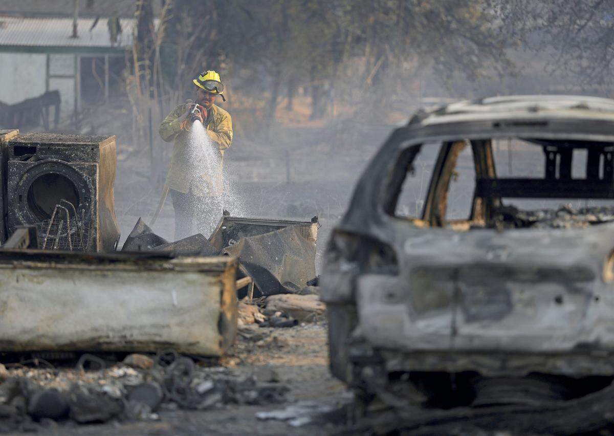 A Cal Fire firefighter sprays water Wednesday on hot spots on a property that was burned by the 6-5 Fire in the TCU September Lightning Complex in Chinese Camp. Nearly 12,000 acres have burned, and several structures were destroyed in the historic Gold Rush town.