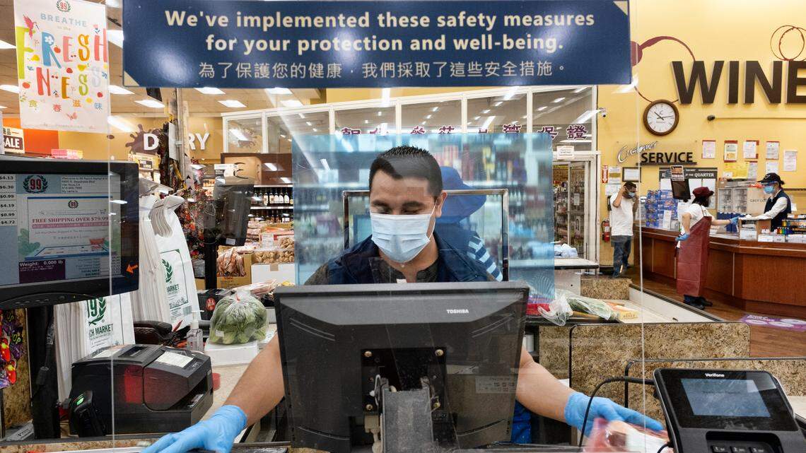 In this May 5, 2020, file photo, a grocery worker, wears a protective mask and gloves, as he helps to check out a customer from behind a plexiglass barrier at a market in the Van Nuys section of Los Angeles. Coronavirus outbreaks and the soaring cases at Southern California supermarkets has ratcheted up anxiety for grocery workers amid the pandemic.