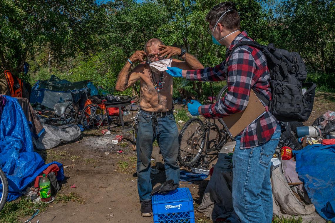 Cal Northstate med student Kirk Carter, helps Robert Teague, 67, adjust a mask he provided at a homeless encampment in Sacramento on Monday, April 13, 2020. UC Davis and Cal Northstate medical students have been providing medical care to homeless people during the coronavirus pandemic. The students are volunteers and although they have coordinated with the county health department they are not getting paid. They are doing this on top of full class loads.