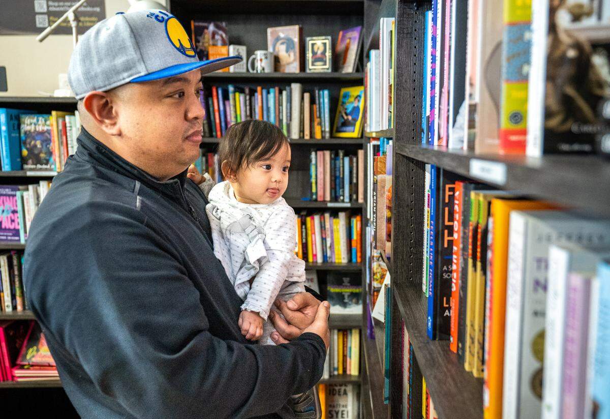 Brandon Wong holds his 10-month-old daughter, Katiya, as they look for something good to read in A Seat at the Table Books in Elk Grove on Tuesday.