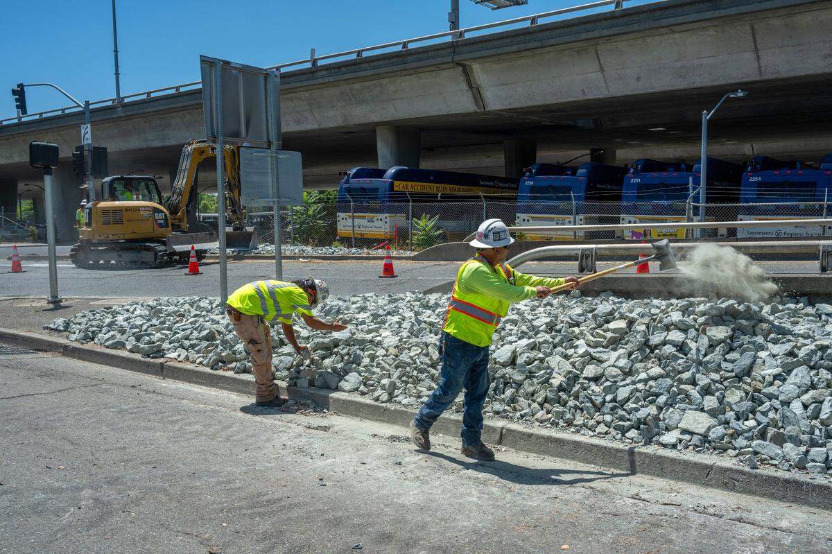 Caltrans workers Anthony Exiga, left, and Raymond Rivera adjust the placement of rocks after they were deposited by heavy equipment near the Capital City Freeway on-ramp at the intersection of 30th and P streets on Wednesday, May 29, 2024.