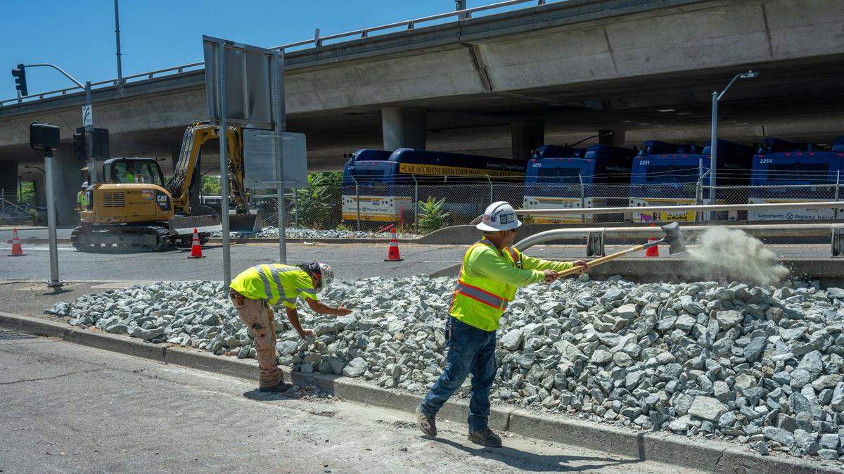Caltrans workers Anthony Exiga, left, and Raymond Rivera adjust the placement of rocks after they were deposited by heavy equipment near the Capital City Freeway on-ramp at the intersection of 30th and P streets on Wednesday, May 29, 2024.