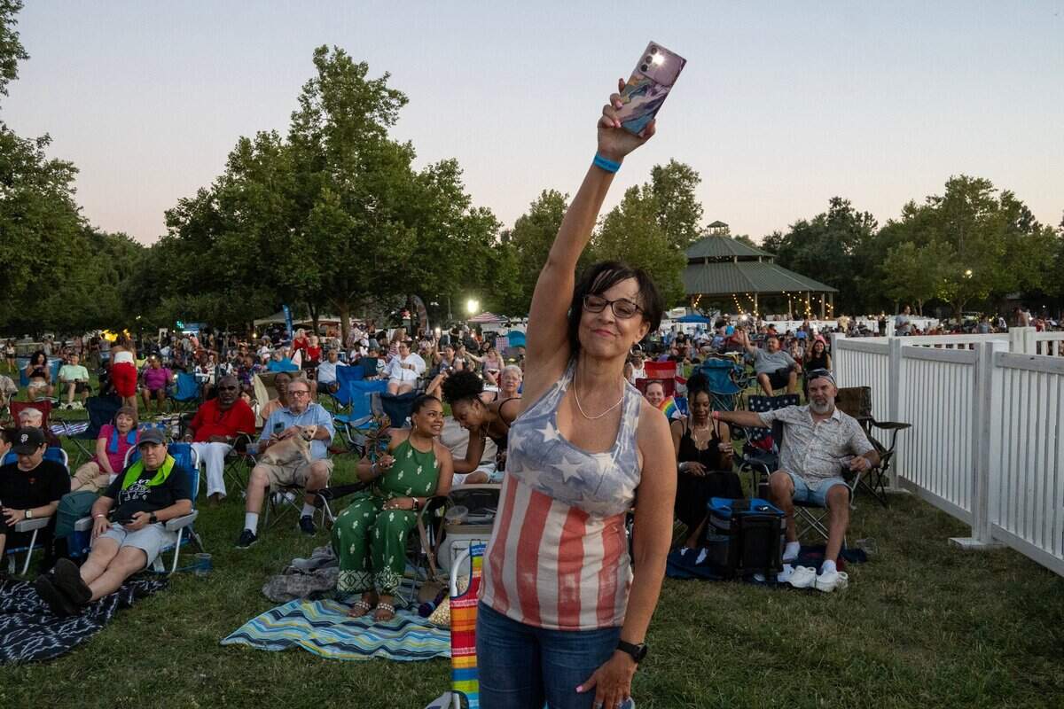 Lizette Young of Roseville waves her cellphone with its light on as she listens to singer Stacy Carter perform the music of Diana Ross at a Fourth of July celebration on Wednesday at Hagan Park in Rancho Cordova.